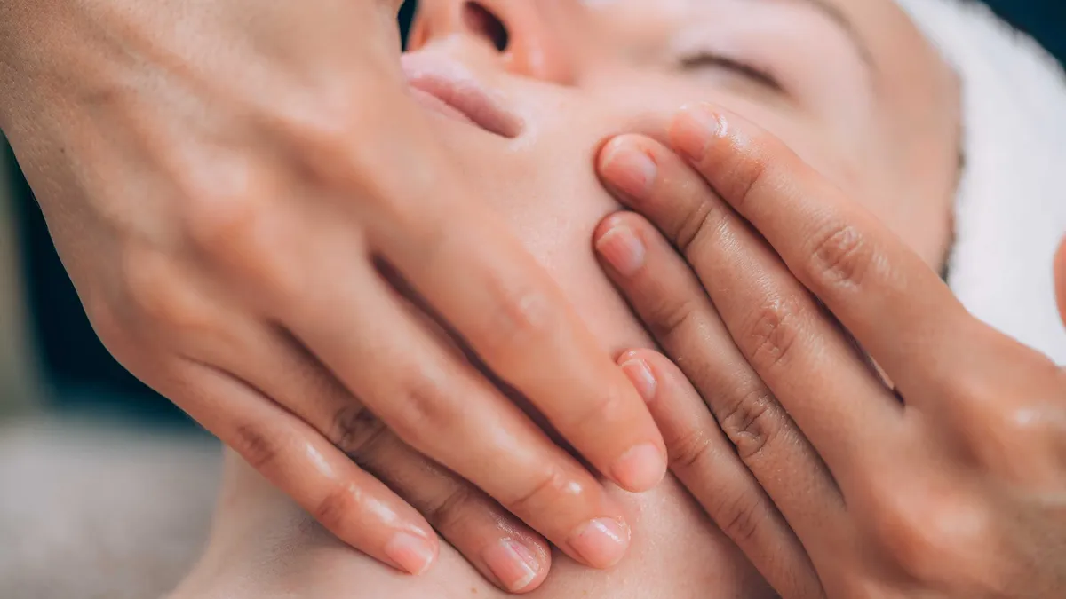 Hands cradling a client's face during reflexology, eyes peacefully closed
